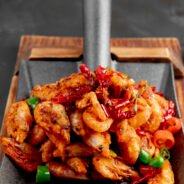 side view of fried shrimps with red and green peppers on a wooden cutting board